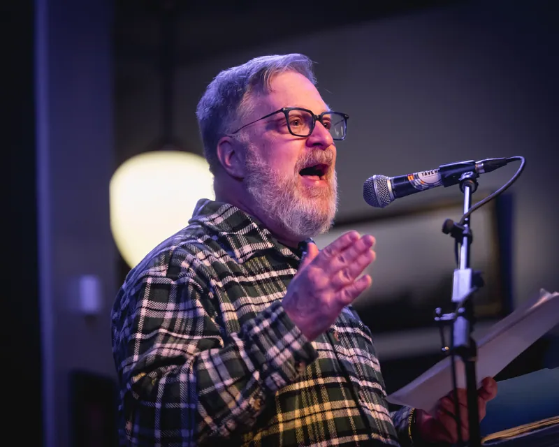 A combatant in plaid reading from his pages at the microphone