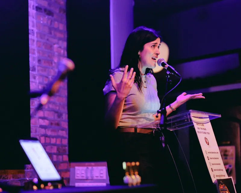A combatant mid-gesture at the lectern under purple light