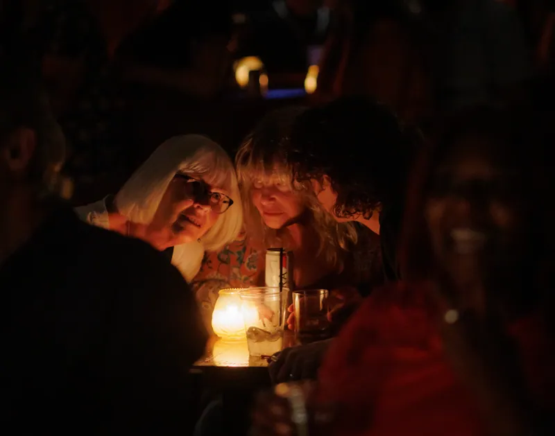 The audience at candlelit tables, faces lit by the flames