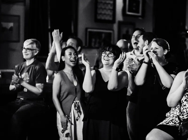 The audience laughing, hands to faces, in black and white