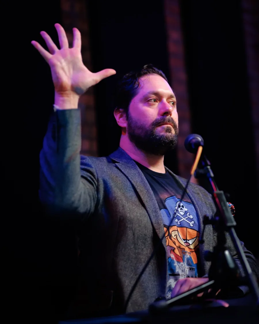 Josh Zagoren at the microphone with a hand raised, palm out