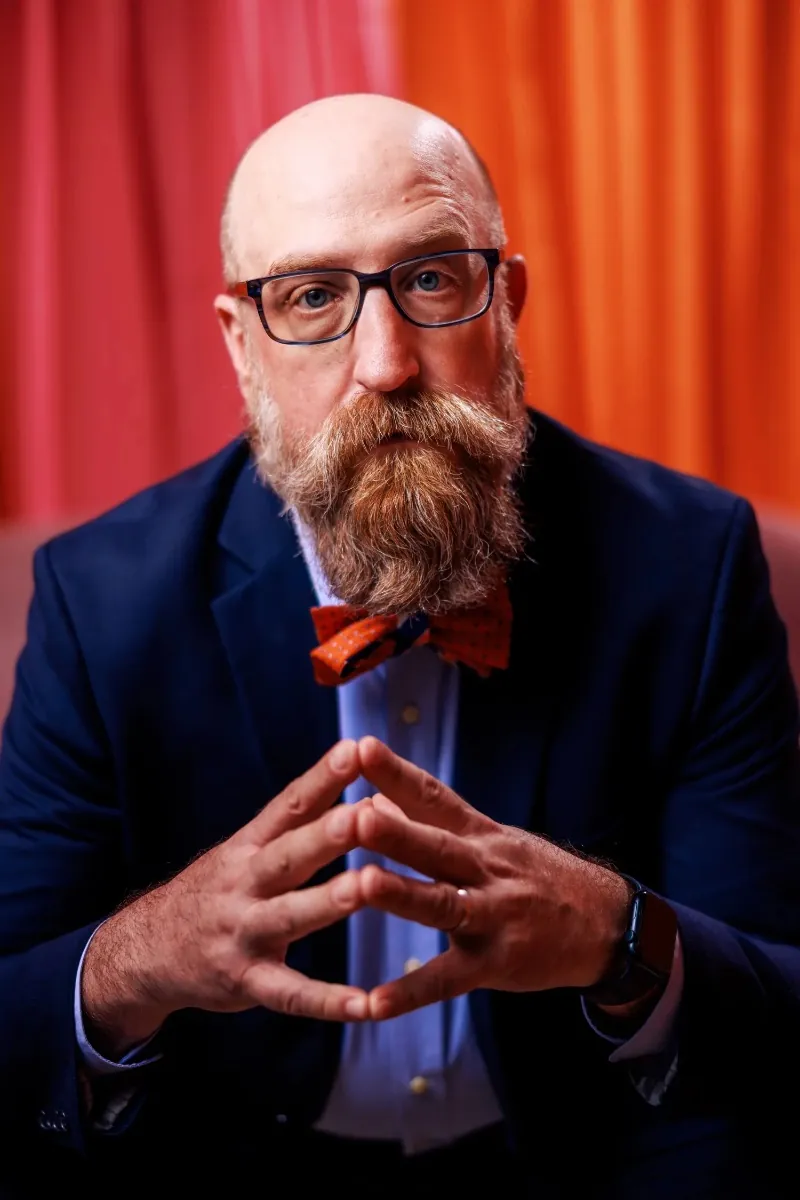 Kyle Hamman in glasses and a bow tie, hands steepled